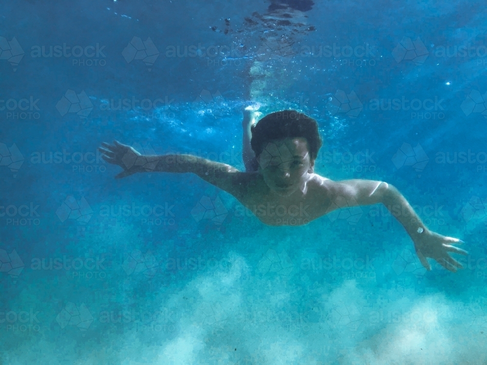 Young boy swimming underwater with sun beams through water - Australian Stock Image