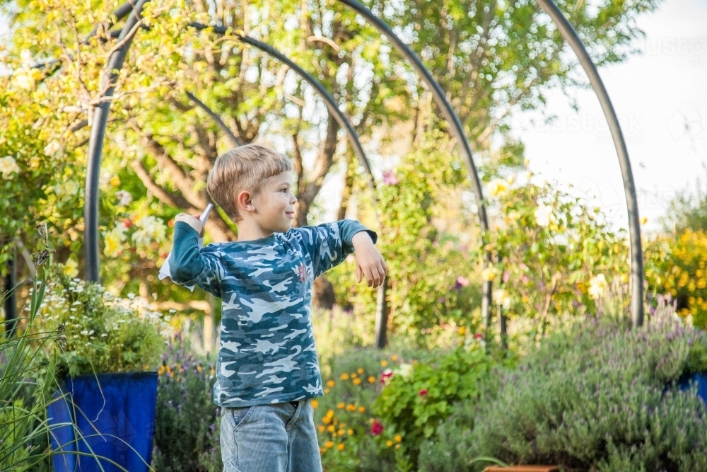 Young boy throwing a paper plane in the backyard - Australian Stock Image