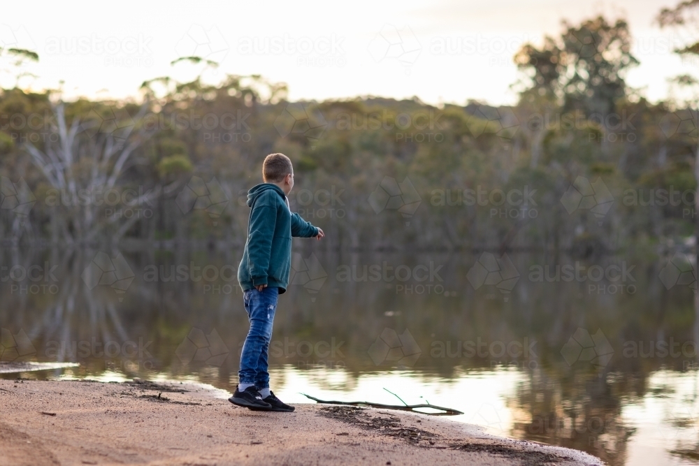young boy throwing a rock into a lake - Australian Stock Image