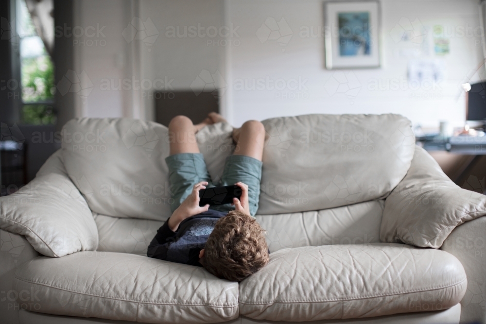 Young boy upside down, playing a video game - Australian Stock Image