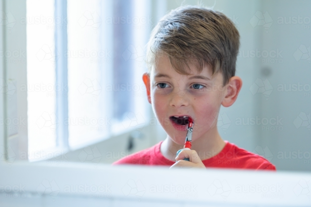 Young boy using electric toothbrush in mirror - Australian Stock Image