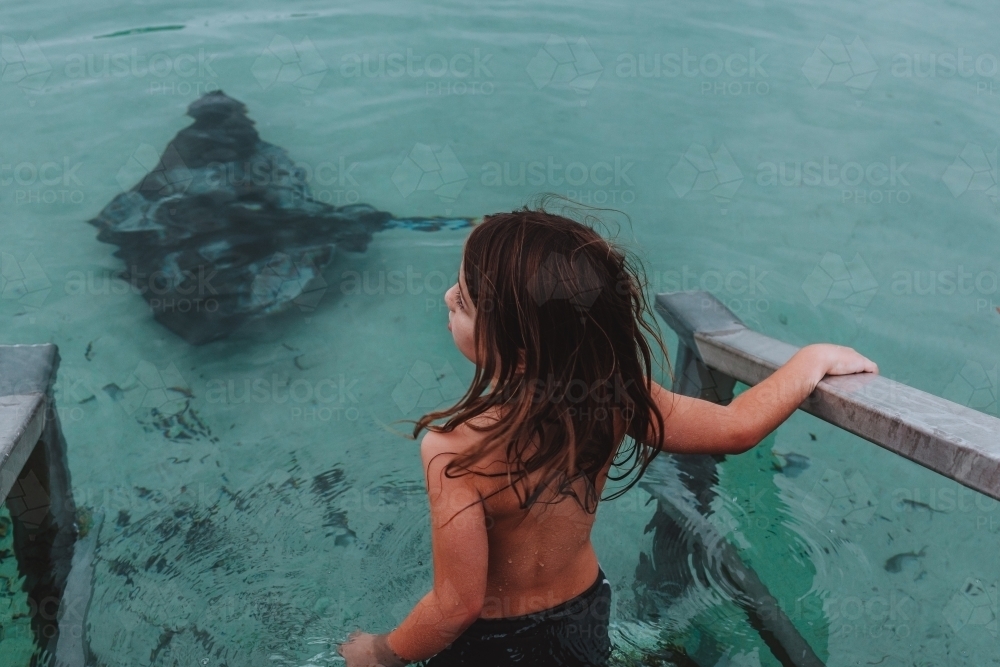 Young boy walking down ocean stairs towards stingray - Australian Stock Image