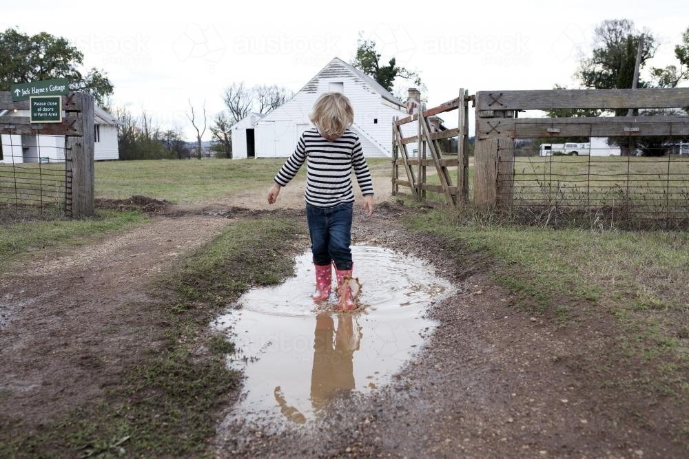 Young boy walking through puddle in gumboots on the farm - Australian Stock Image