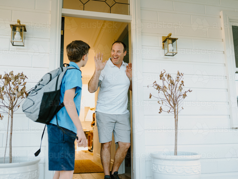 Young boy waving his hand goodbye to his dad at the doorway. - Australian Stock Image
