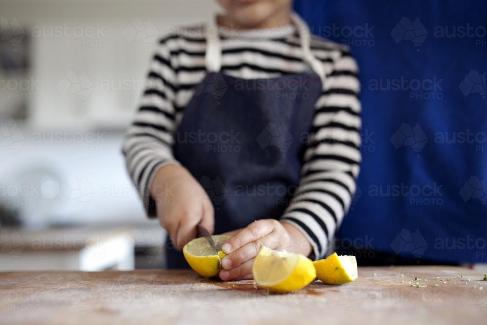 Young boy wearing apron cutting lemons - Australian Stock Image