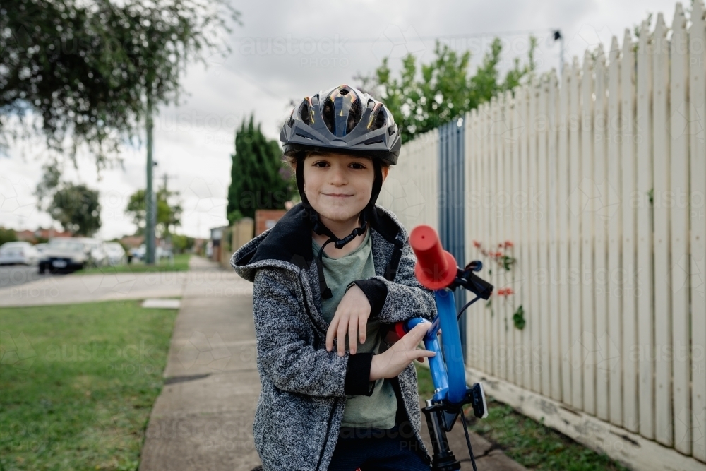 Young boy wearing bike helmet poses for a portrait on his bicycle; cycling around his neighbourhood - Australian Stock Image