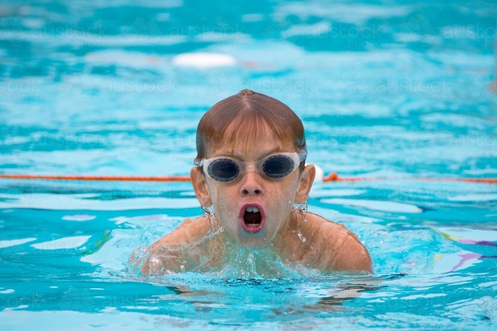 Young boy wearing goggles swimming breaststroke in swimming pool - Australian Stock Image