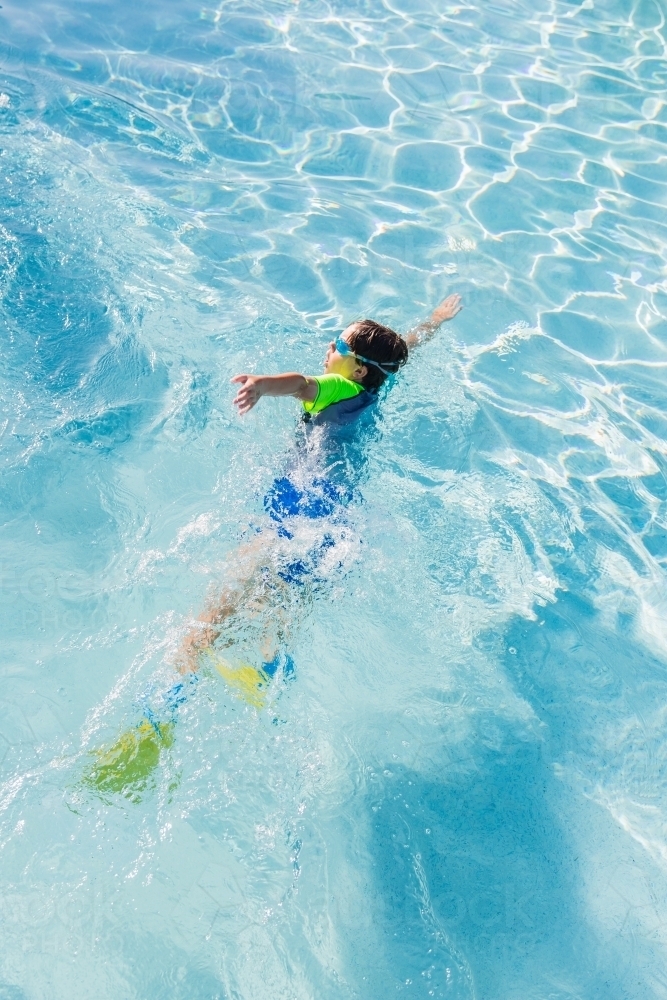 Young boy wearing googles and flippers swimming in pool - Australian Stock Image