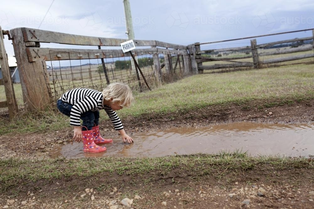 Young boy wearing gumboots playing in muddy puddle - Australian Stock Image