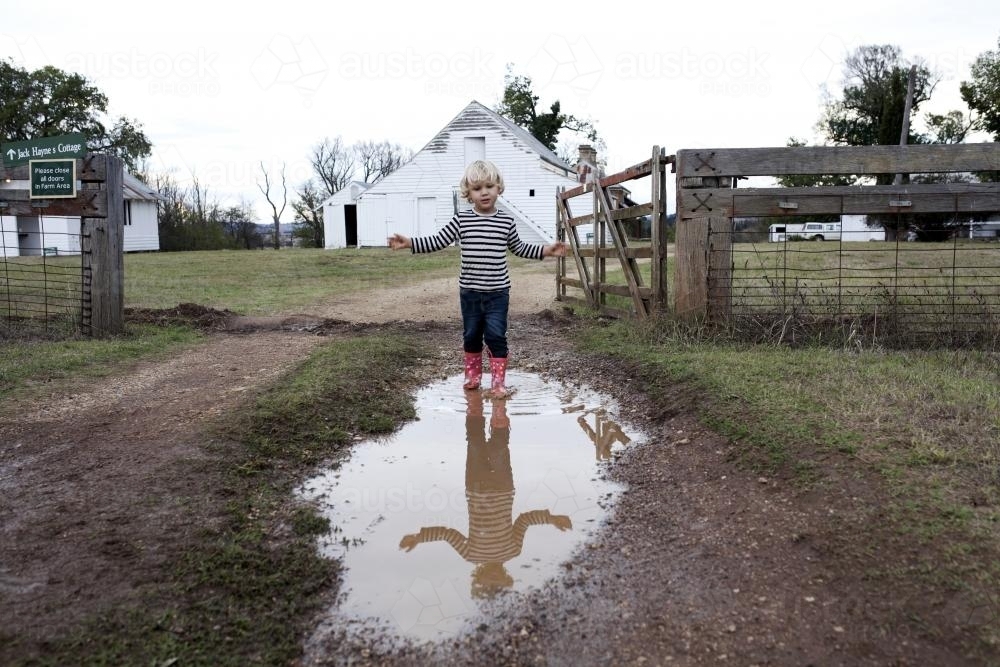 Young boy wearing gumboots walking through muddy puddle - Australian Stock Image