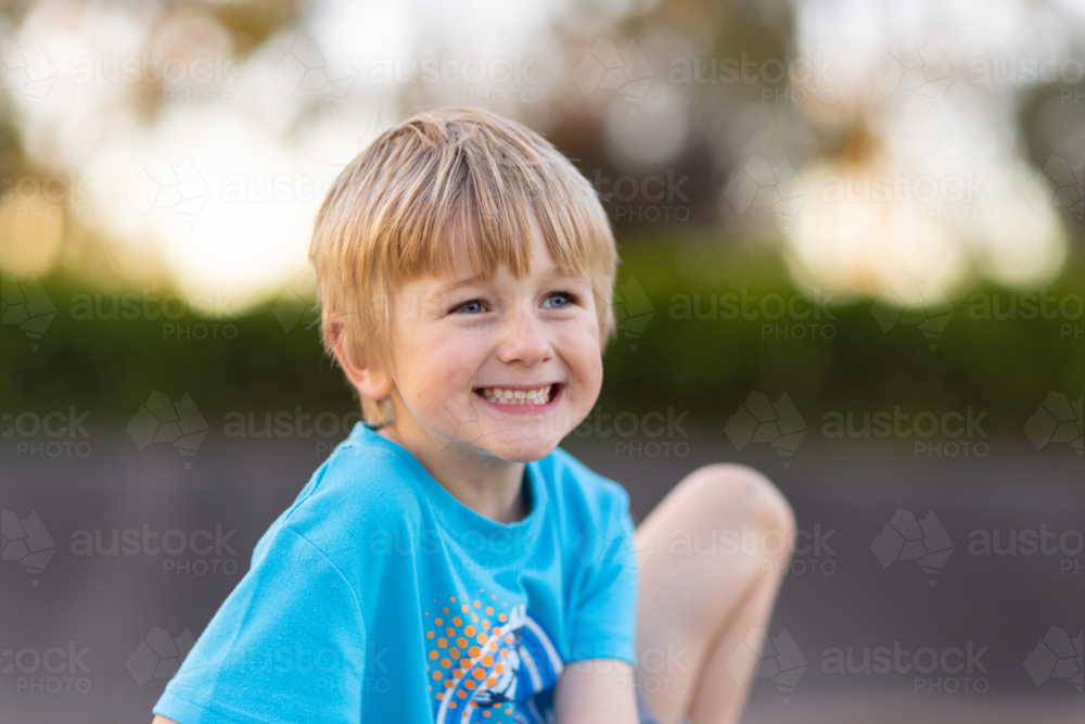 young boy with a big cheesy grin on his face outside with blurry background - Australian Stock Image