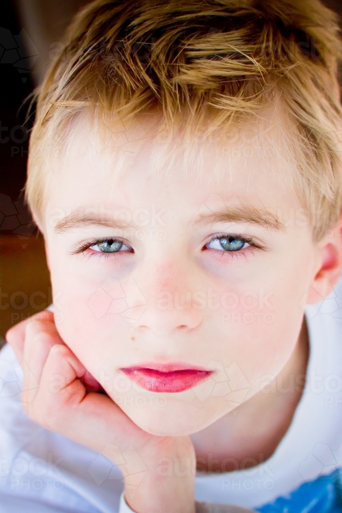 Young boy with blonde hair resting his head on his hand - Australian Stock Image