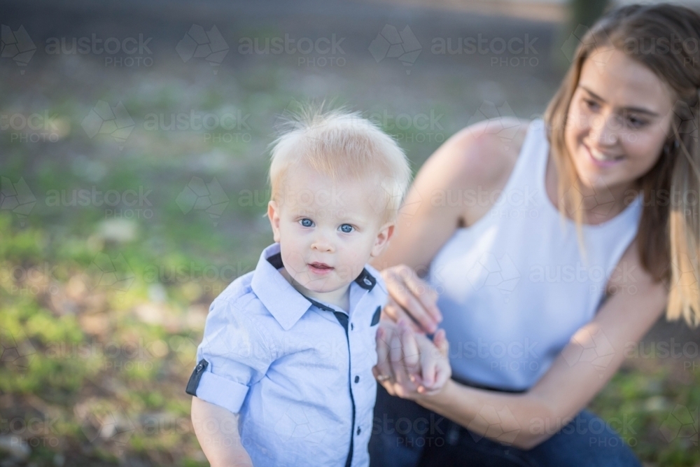 Young boy with blue eyes standing holding hands with mother - Australian Stock Image