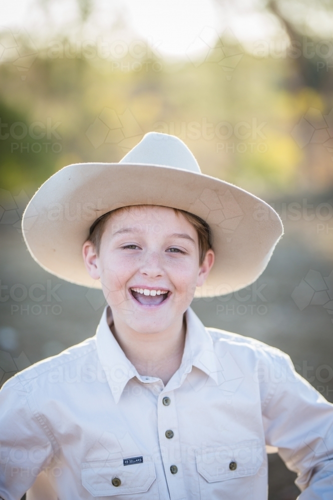 Young boy with cheeky smile wearing akubra hat on farm in drought - Australian Stock Image