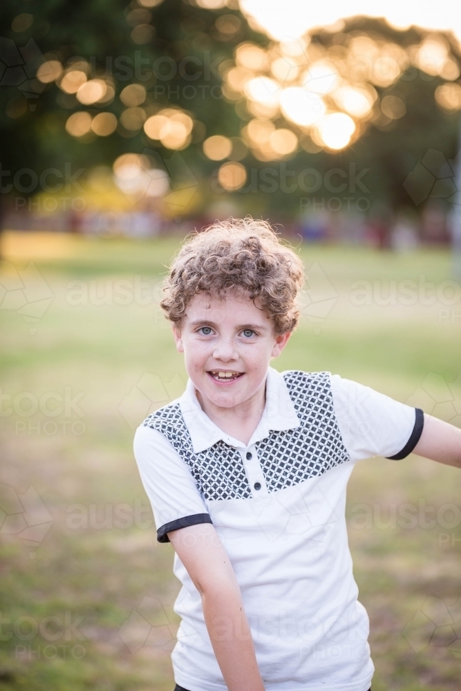 Young boy with curls dancing in park - Australian Stock Image