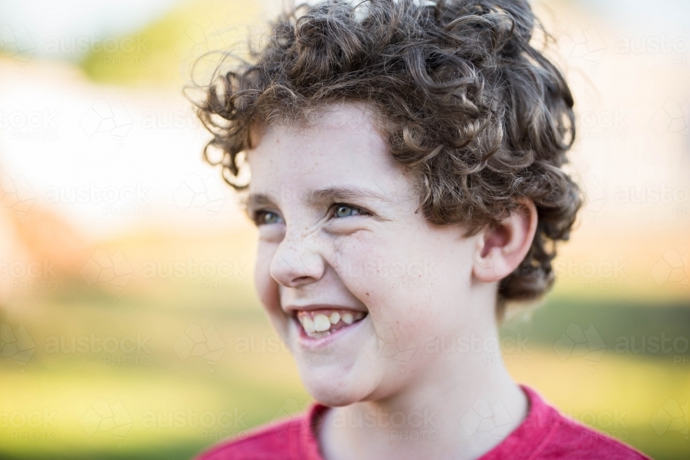 Young boy with curly hair laughing looking away - Australian Stock Image