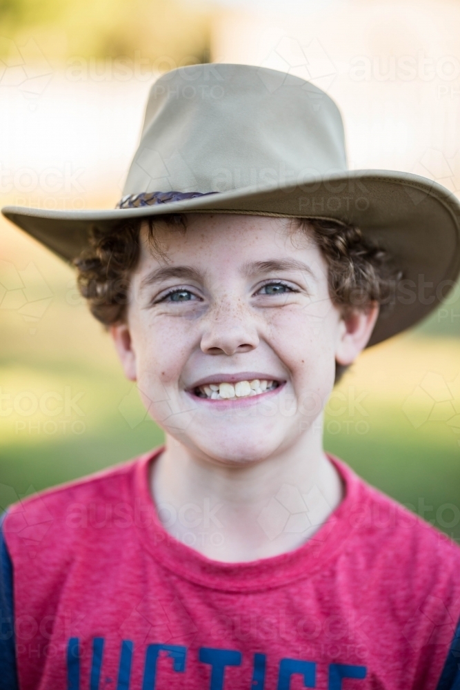 Young boy with curly hair wearing akubra hat smiling - Australian Stock Image