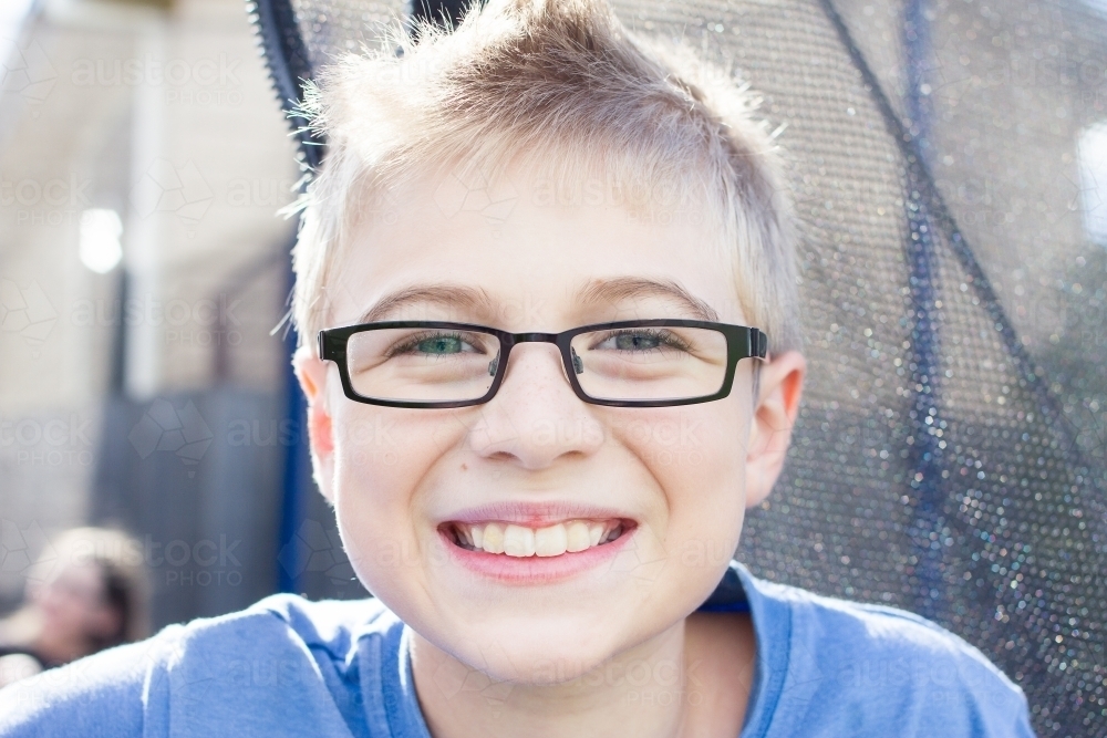 Young boy with glasses sitting on trampoline - Australian Stock Image