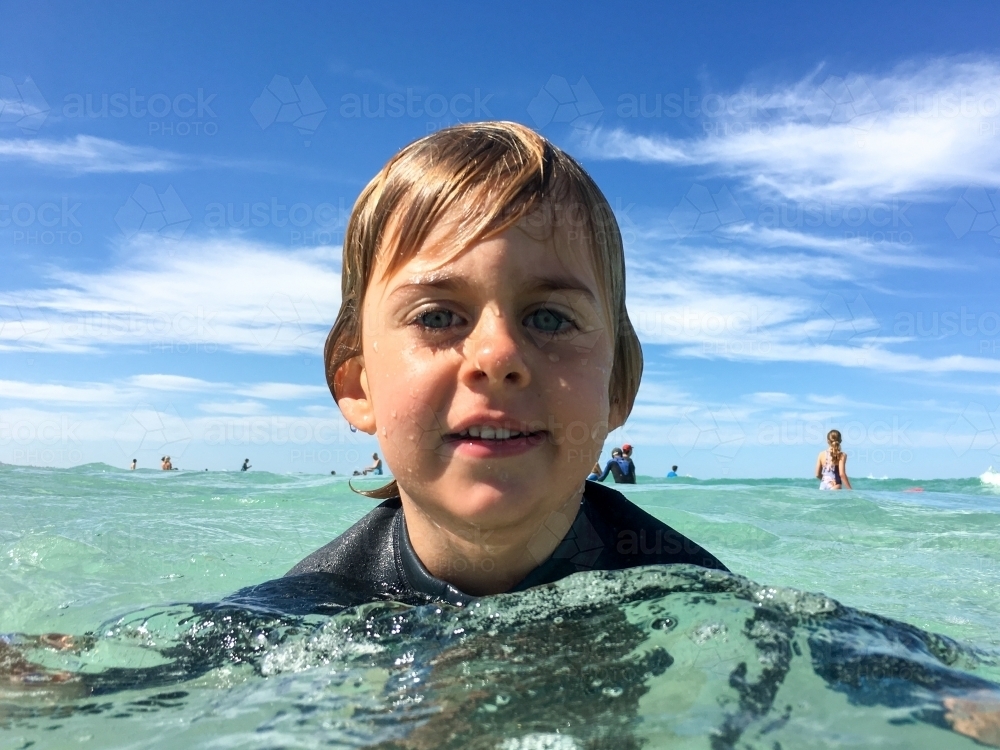 Young boy with head above water in ocean looking at camera - Australian Stock Image