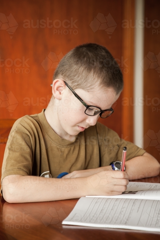 Young boy writing in his school work book with a pencil - Australian Stock Image
