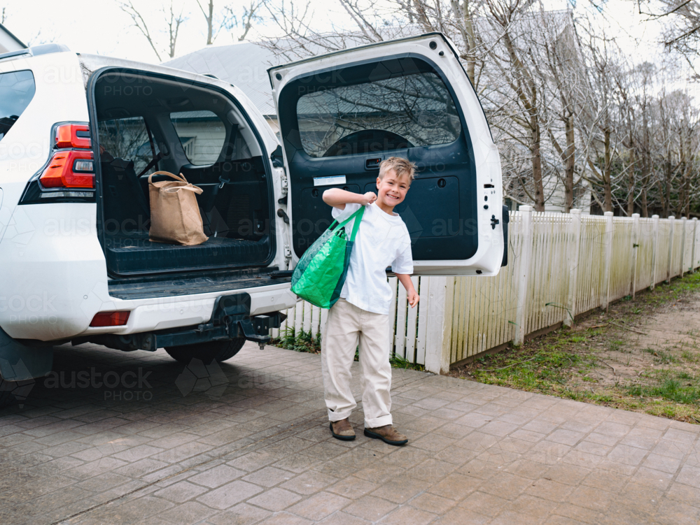 Young boys carrying green shopping bag out of car boot - Australian Stock Image