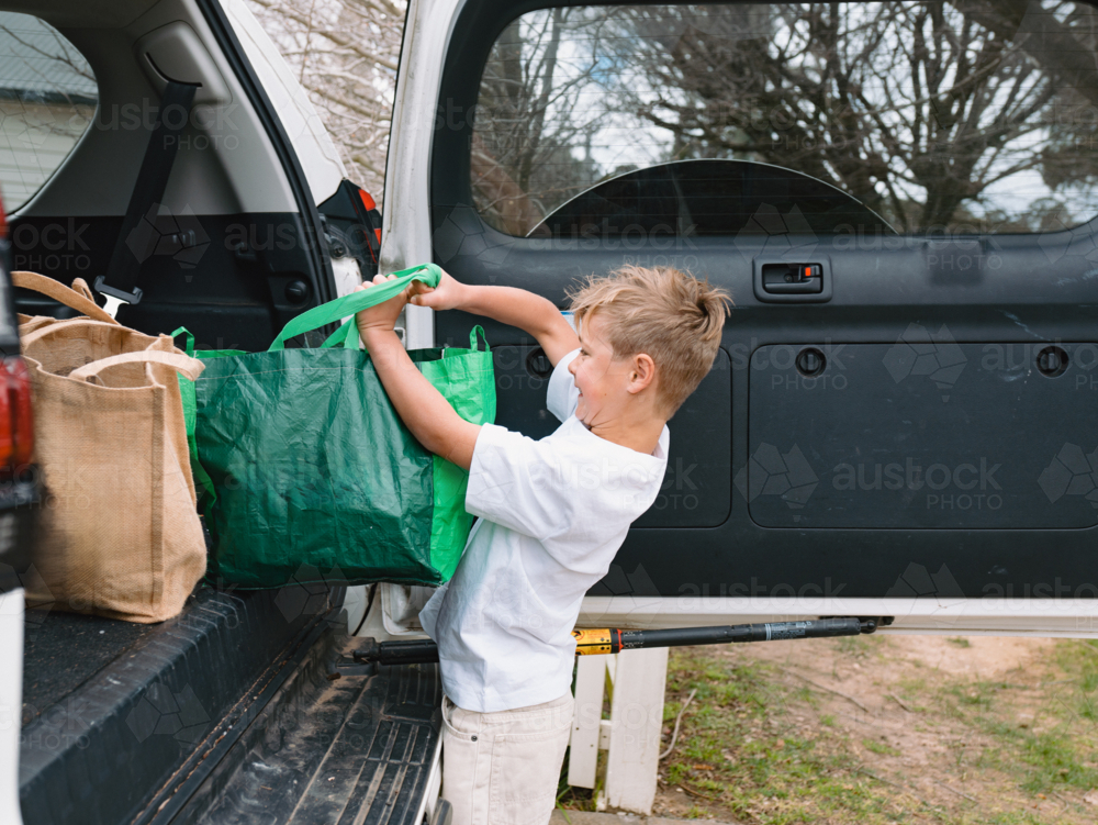 Young boys carrying green shopping bags out of car boot - Australian Stock Image
