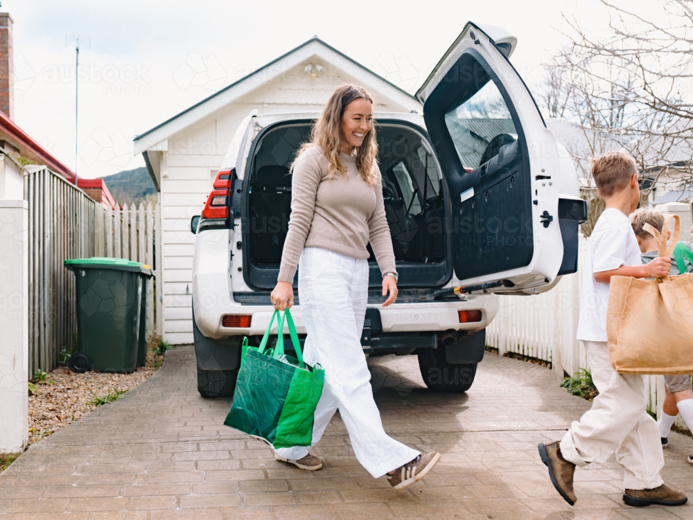 Young boys helping mum carry grocery bags from car boot - Australian Stock Image
