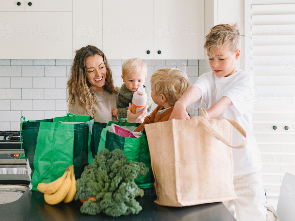 Young boys helping mum take the groceries out of the shopping bag in the countertop - Australian Stock Image