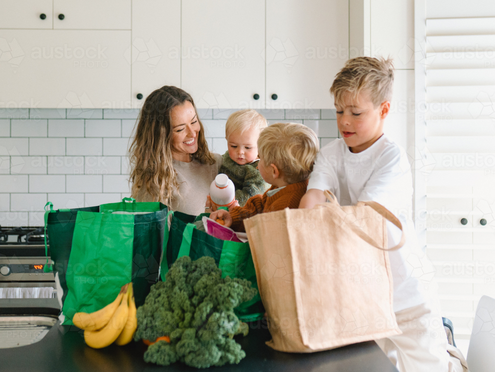 Young boys helping mum take the groceries out of the shopping bag in the countertop - Australian Stock Image