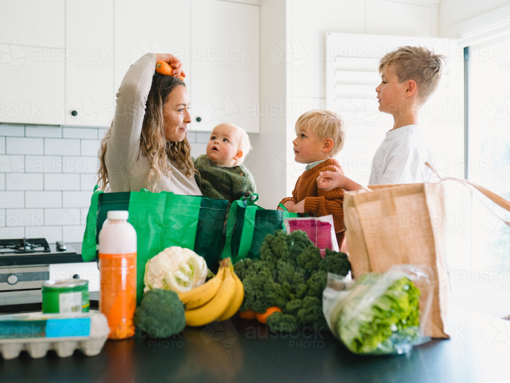 Young boys helping mum take the groceries out of the shopping bag in the countertop - Australian Stock Image