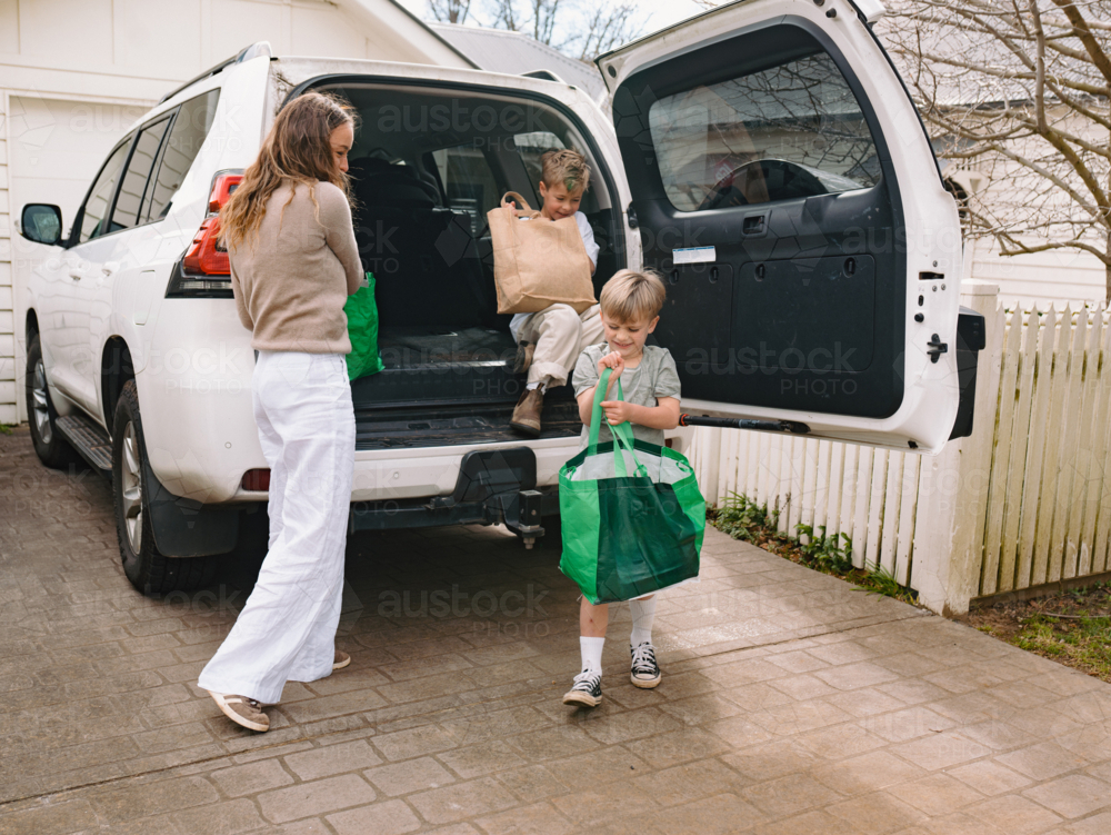 Young boys helping mum unload grocery bags from car boot - Australian Stock Image