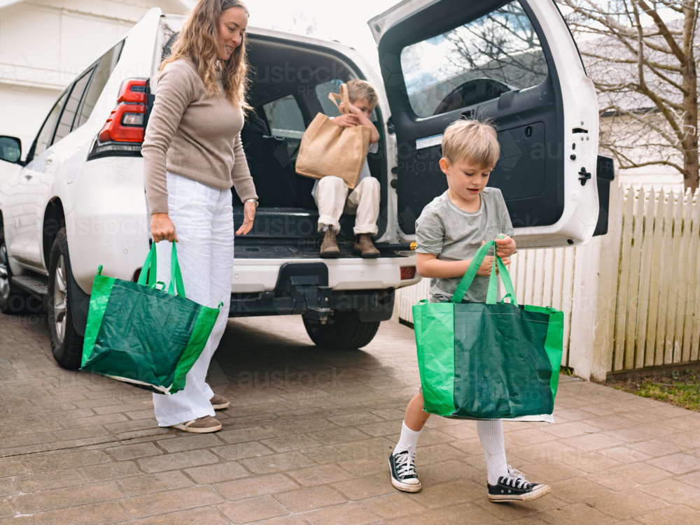 Young boys helping mum unload grocery bags from car boot - Australian Stock Image