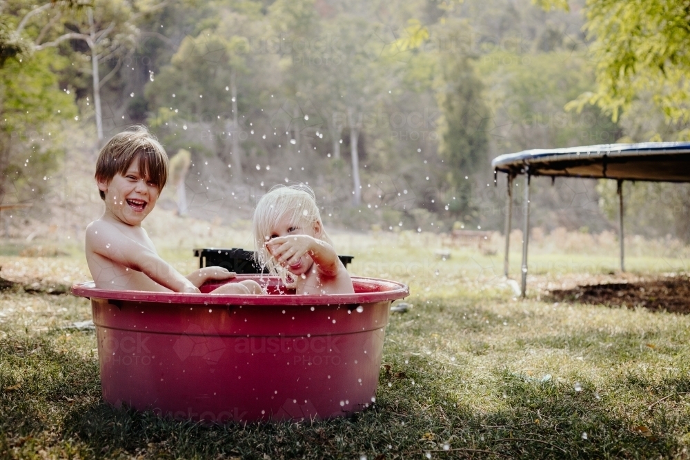 Young boys playing in a tub of water outside on a hot day - Australian Stock Image