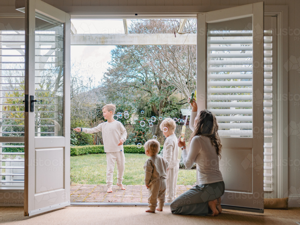 Young boys playing in the patio with mum kneeling by the doorway - Australian Stock Image