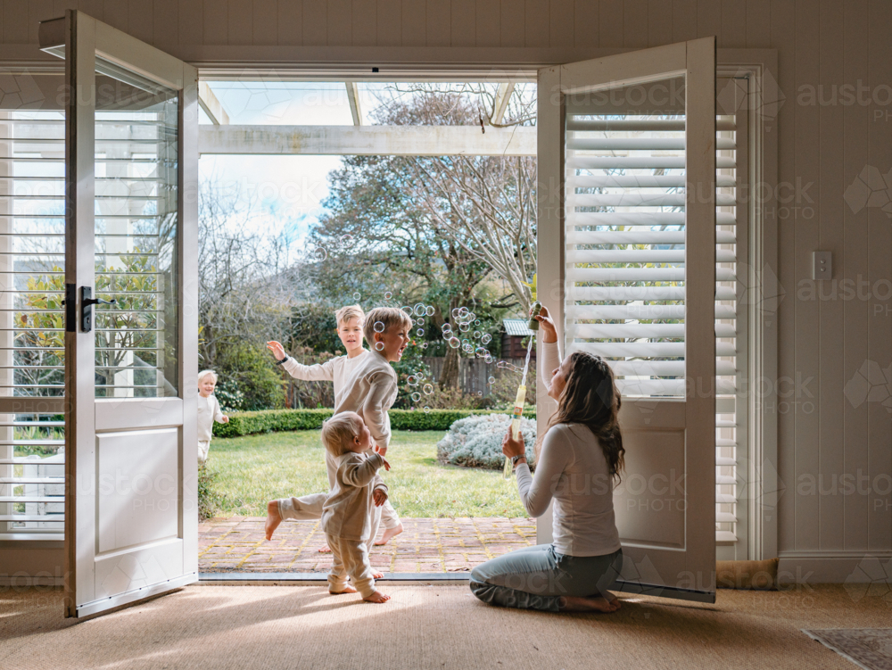 Young boys playing in the patio with mum kneeling by the doorway - Australian Stock Image