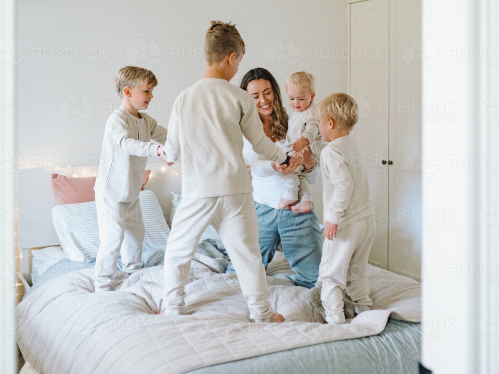 Young boys playing on the bed with mum holding baby brother - Australian Stock Image