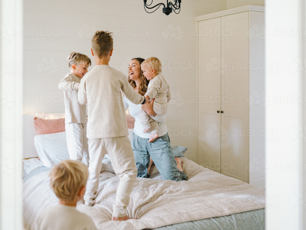Young boys playing while holding hands on the bed with mum holding the baby - Australian Stock Image
