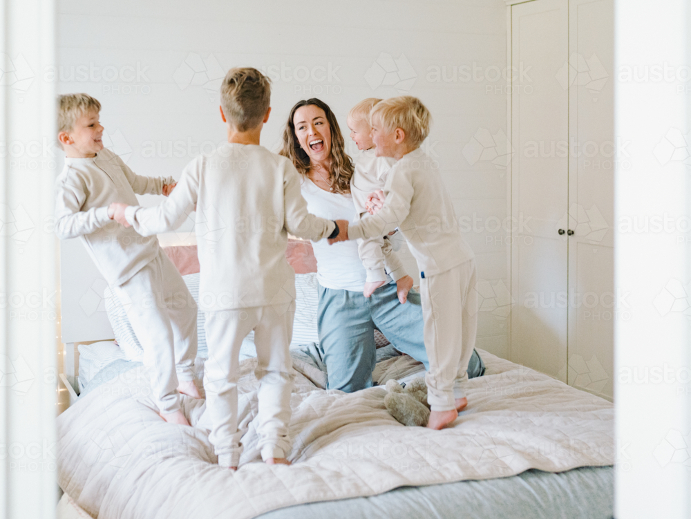 Young boys playing while holding hands on the bed with mum holding the baby - Australian Stock Image