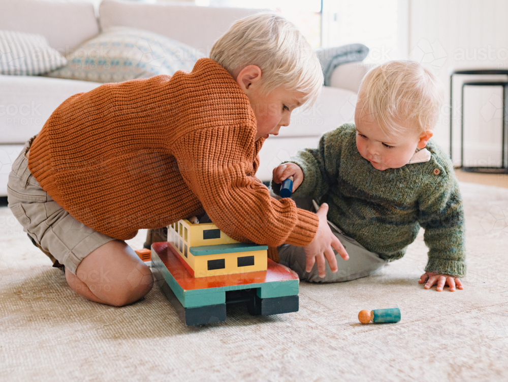 Young boys playing with wooden ferry toy on carpeted floor - Australian Stock Image