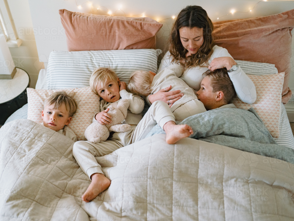 Young boys snuggling with mum on the bed - Australian Stock Image