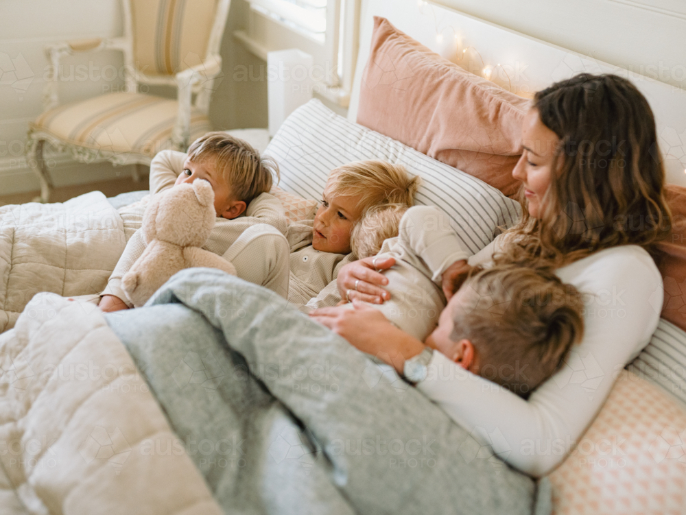 Young boys snuggling with mum on the bed - Australian Stock Image