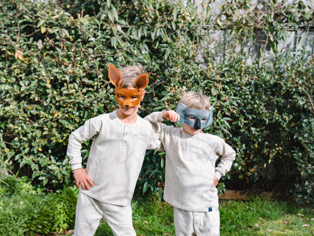 Young boys wearing animal masks standing in front green foliage - Australian Stock Image