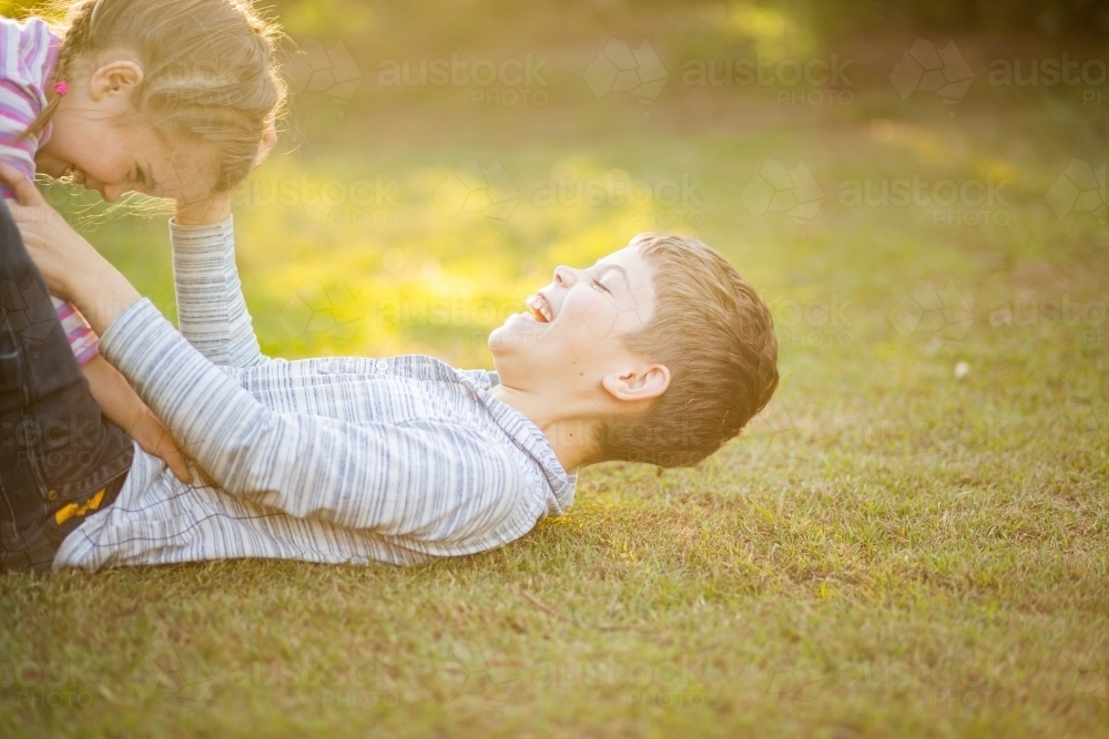 Image of Young brother and sister wrestling on the lawn outside in