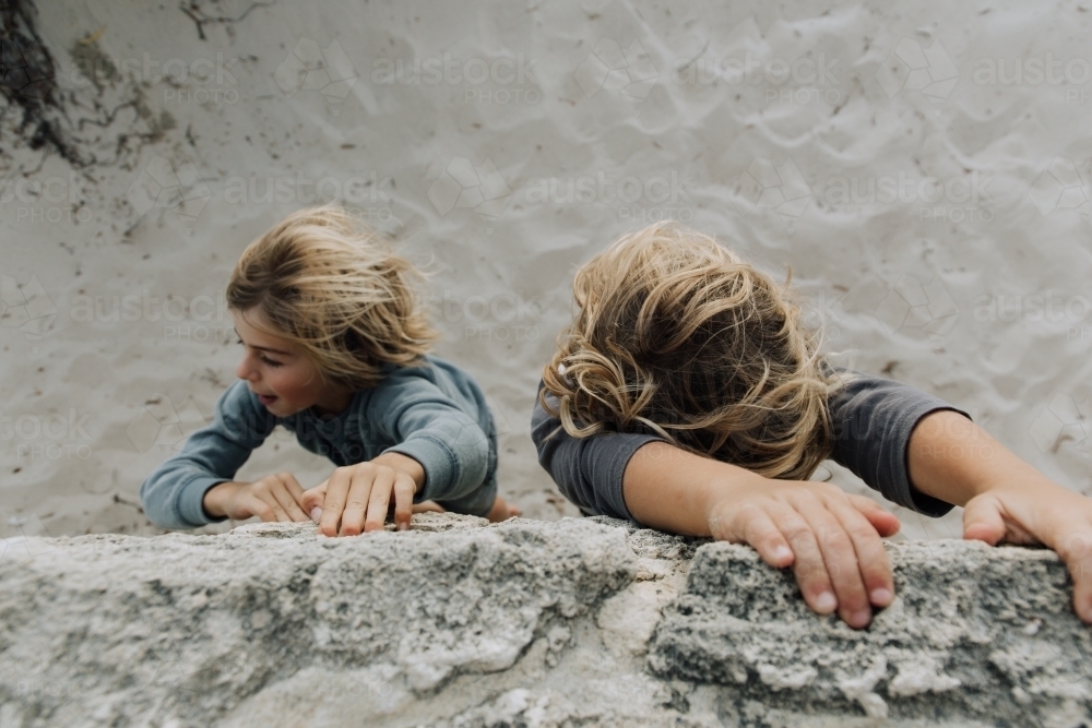 Young brothers climbing wall at beach - Australian Stock Image