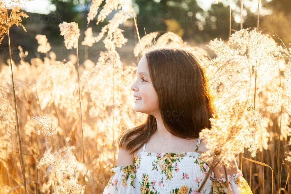 Young brunette girl looking off into the distance backlit by golden light - Australian Stock Image