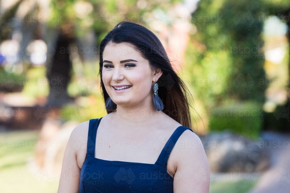 Young brunette woman in early 20s standing in garden smiling - Australian Stock Image