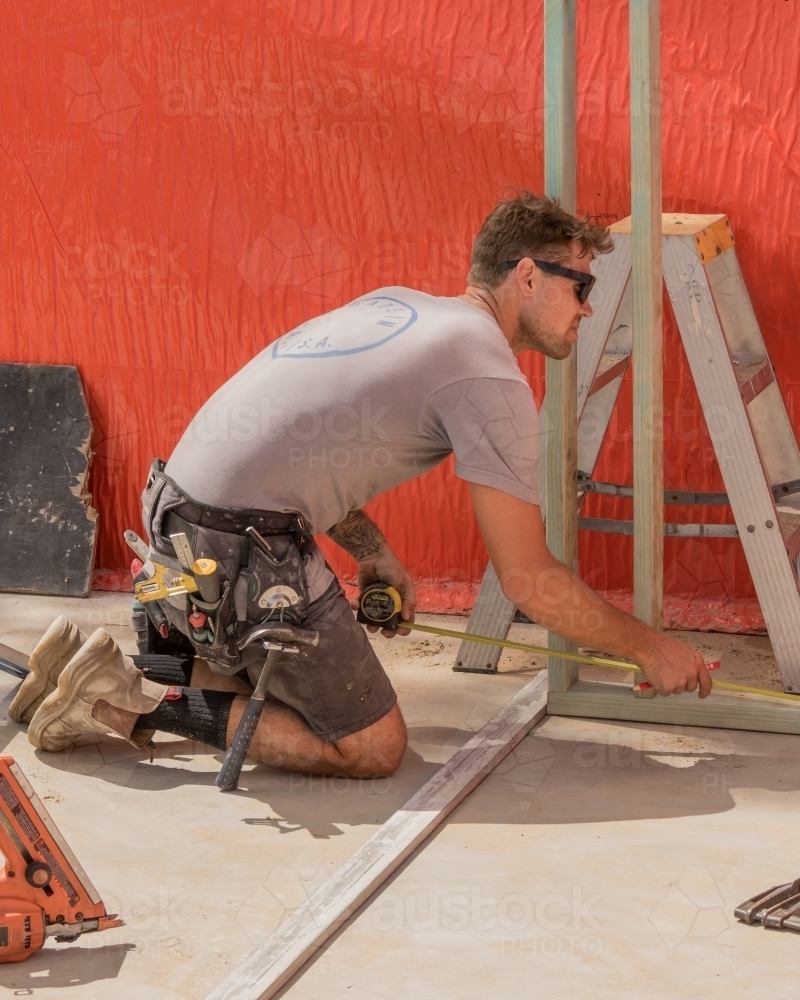 Young builder using tape measure on residential construction site - Australian Stock Image