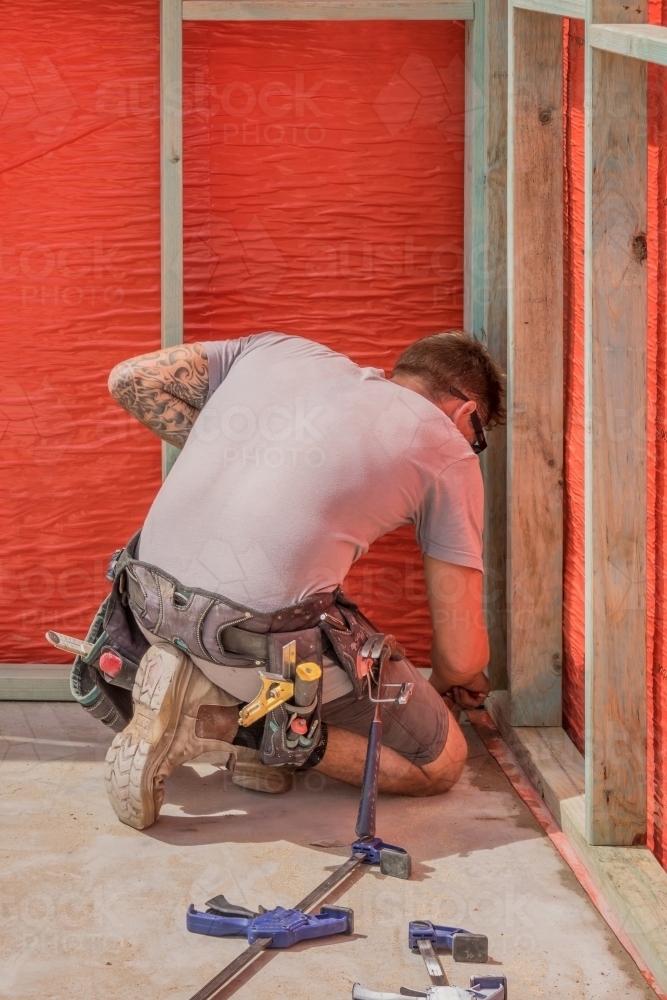 Young builder using tape measure on residential construction site - Australian Stock Image