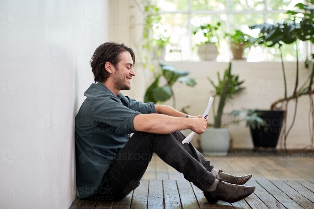 Young business man relaxing sitting on a timber floor in studio - Australian Stock Image