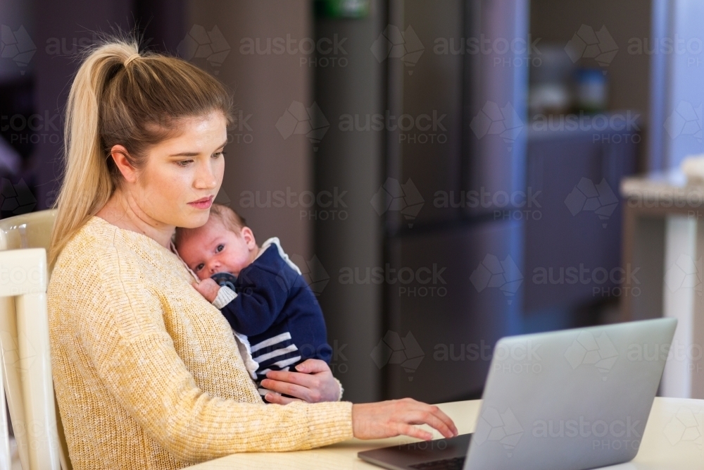 Young businesswoman mum working from home on laptop with newborn baby - Australian Stock Image